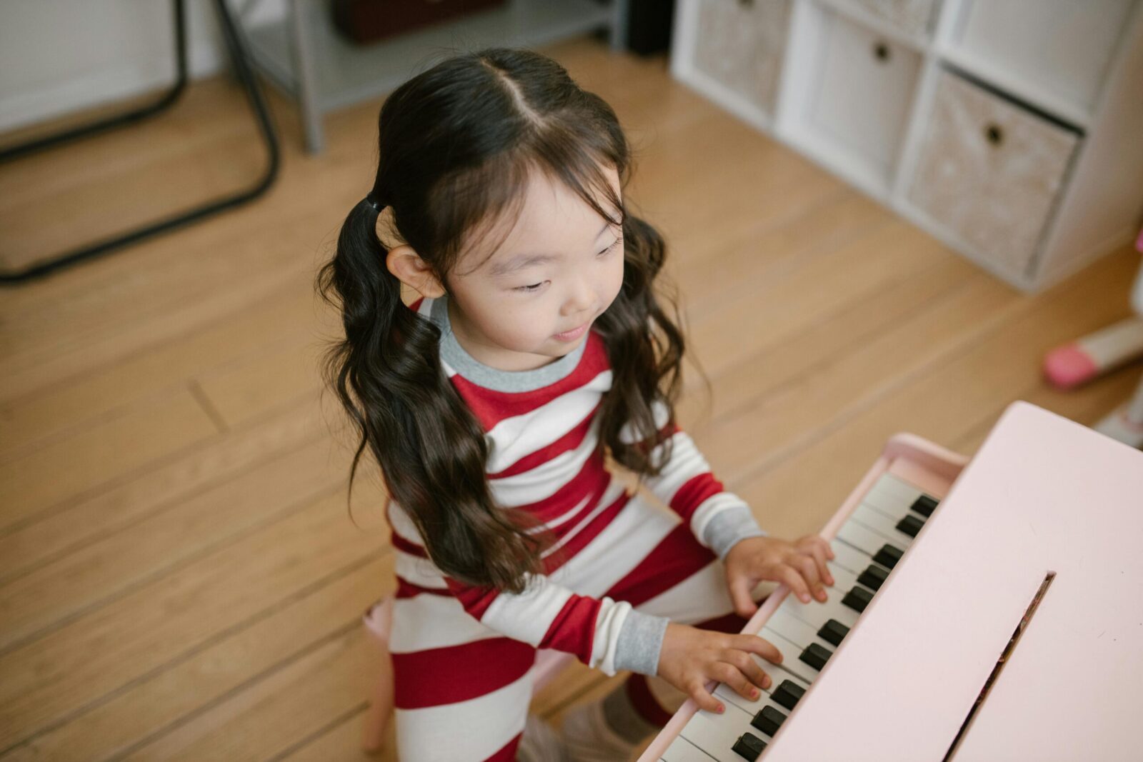 A young girl in pajamas plays a toy piano in a cozy home setting, exuding innocence and creativity.